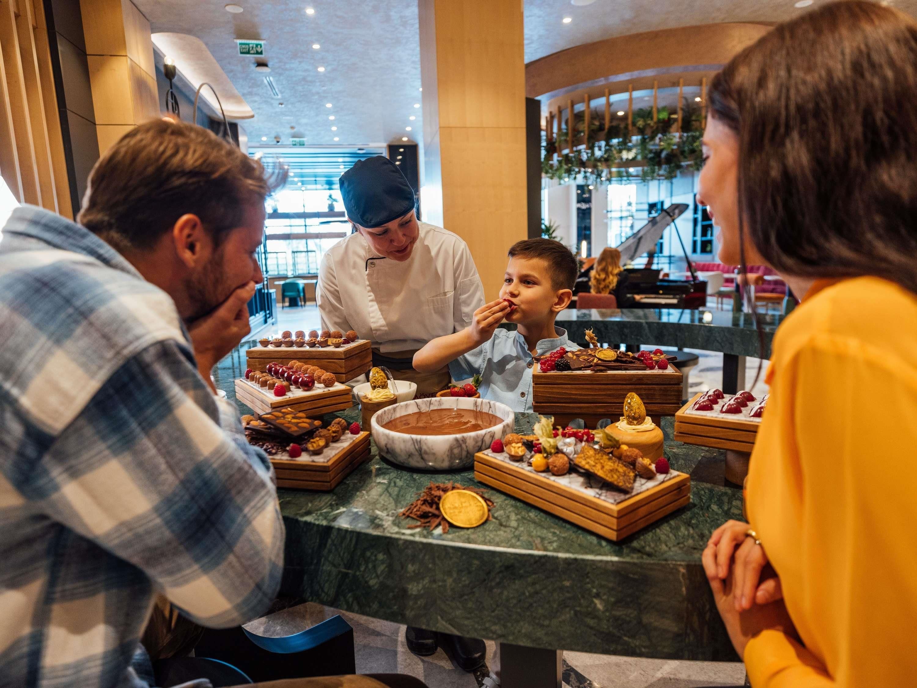 Een groep mensen zit aan tafel met diverse desserts en een kok die eten serveert.