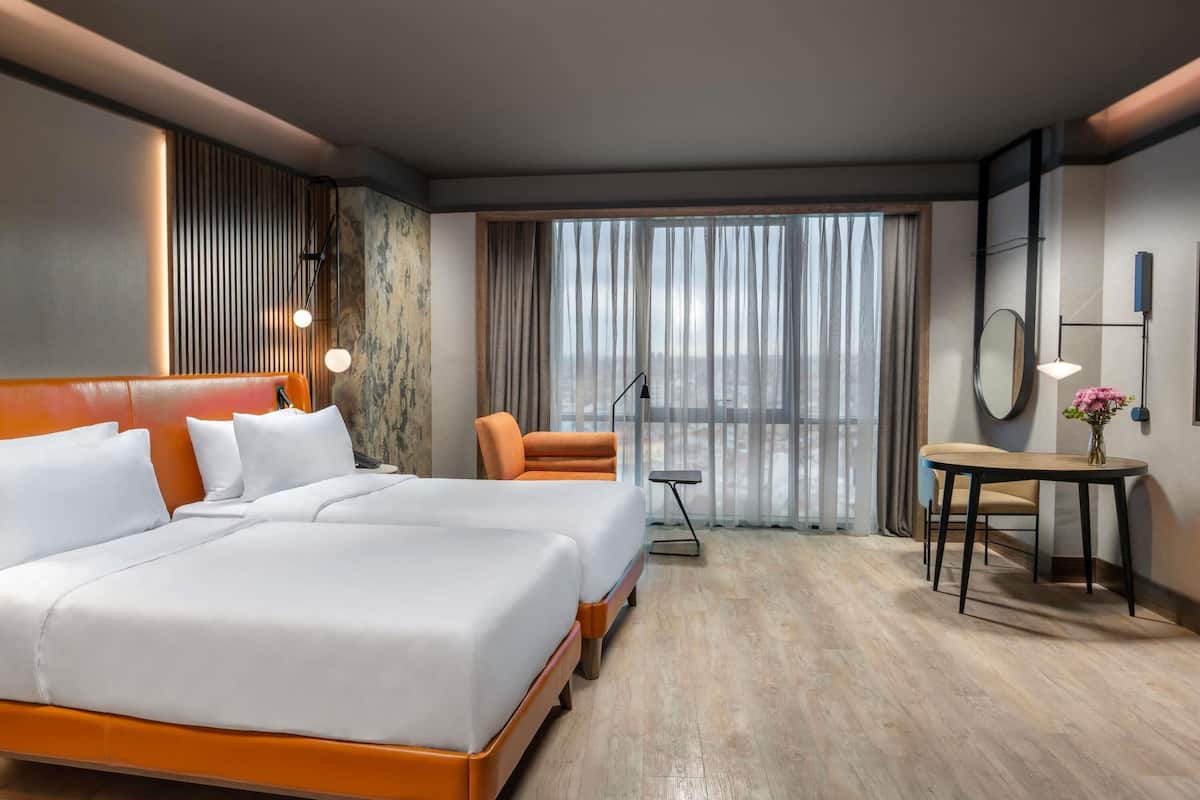 A hotel room with a large bed, a desk, a chair, and a view of the city through the window.