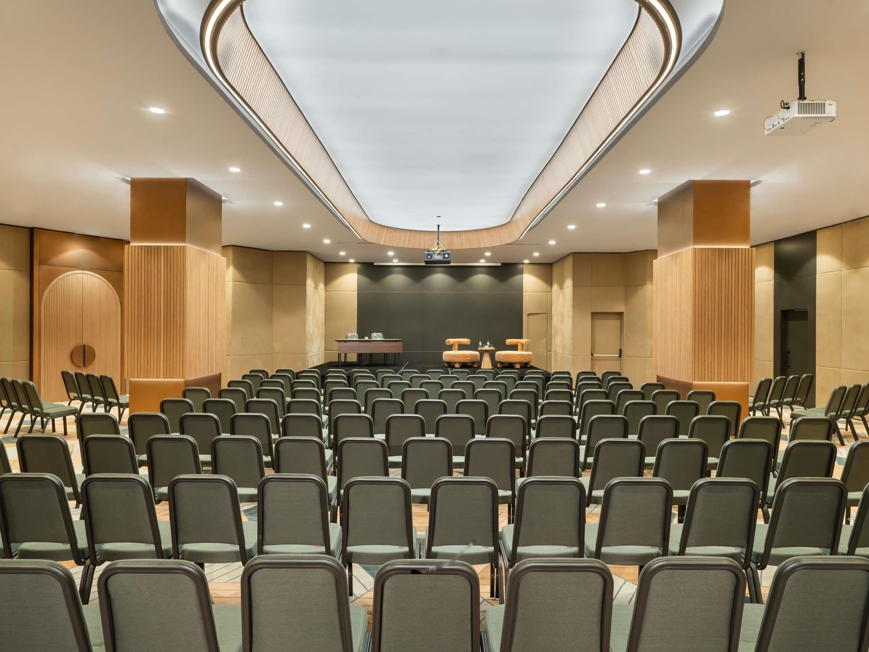 Una sala conferenze con file di sedie, un palco con un leggio e un proiettore a soffitto.