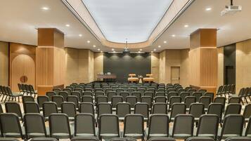 Una sala conferenze con file di sedie, un palco con un leggio e un proiettore a soffitto.