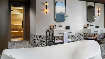 Un bagno moderno con una vasca freestanding, due lavandini con specchi e una sauna visibile attraverso una porta aperta.