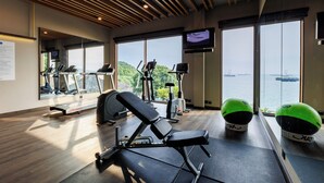 A gym with exercise equipment, large windows, and a view of the water. - Novotel Koh Si Chang (Ko Sichang)