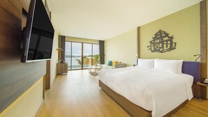 A modern hotel room with a large bed, a flat-screen TV mounted on the wall, a balcony with a view, and a decorative wall piece. - Novotel Koh Si Chang (Ko Sichang)
