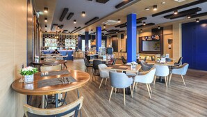 A modern restaurant with wooden tables and chairs, a bar area, and blue accents. - Novotel Koh Si Chang (Ko Sichang)