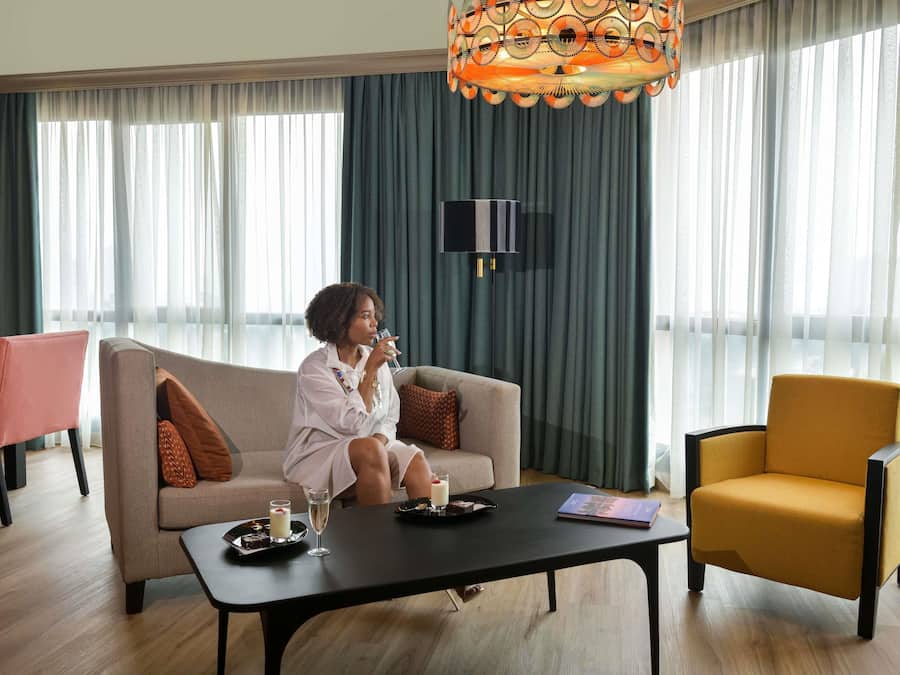 Una habitación de hotel moderna con un sofá, una mesita de centro con un libro, una lámpara decorativa y un televisor.