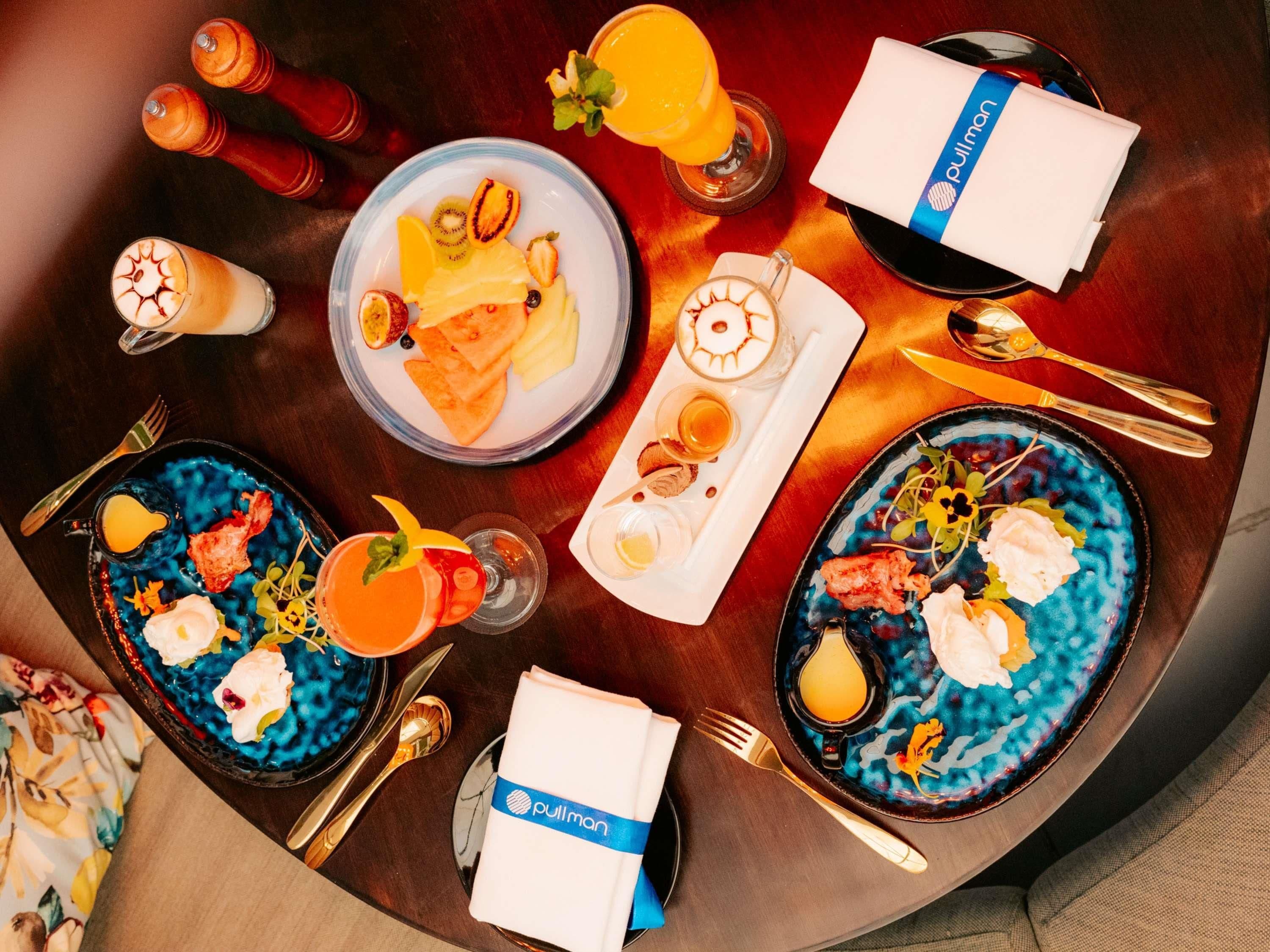 Disposição para o pequeno-almoço com pratos de comida, bebidas e talheres sobre uma mesa de madeira.