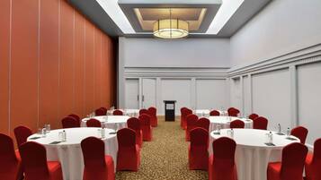 Un salón de conferencias con mesas redondas, sillas rojas y una alfombra estampada.