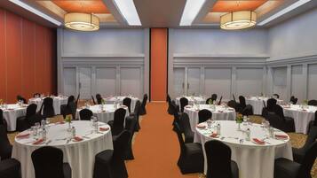 Un salón de conferencias con varias mesas redondas, sillas negras e iluminación en el techo.