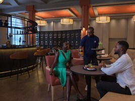 A modern bar area with a curved counter, seating with orange chairs, and a decorative wall with a lattice pattern.