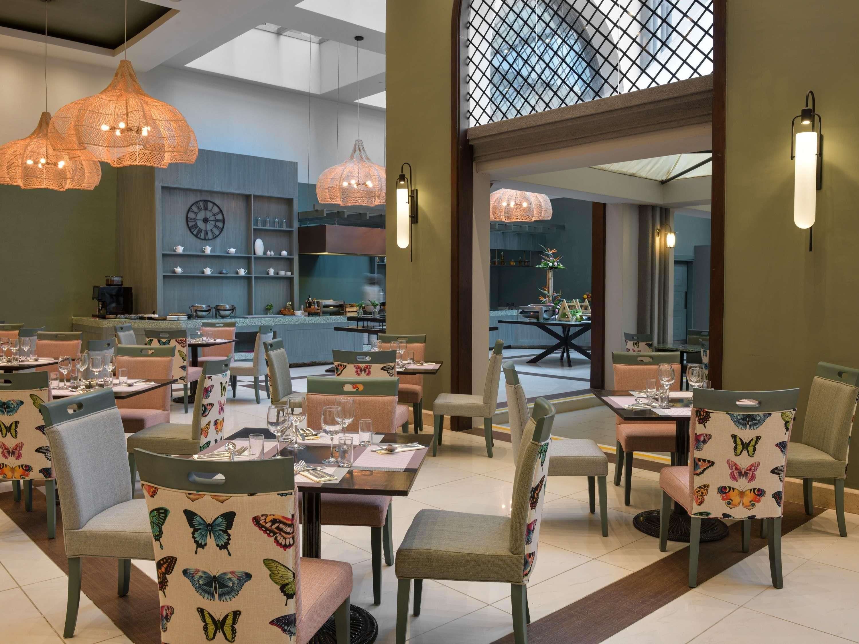 A restaurant with butterfly-patterned chairs, pendant lights, and a view of the kitchen.