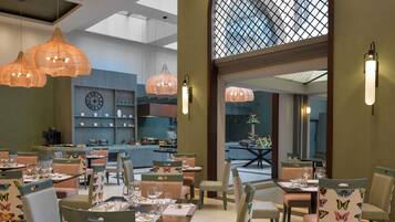 Un restaurante con sillas estampadas con motivos de mariposas, luces colgantes y vista a la cocina.