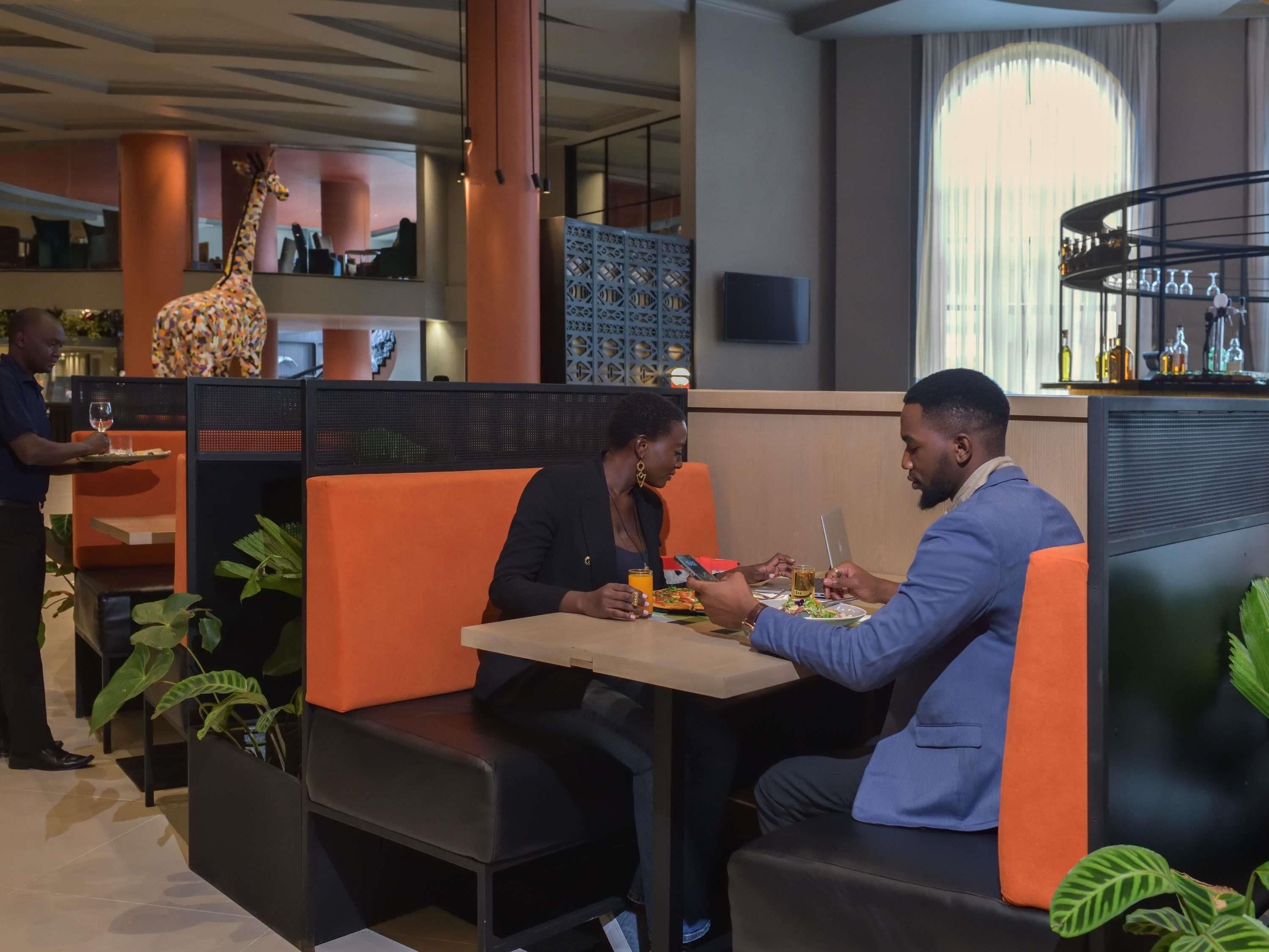 Un comedor moderno con asientos tipo cabina color naranja, una escultura de jirafa y una barra con botellas.