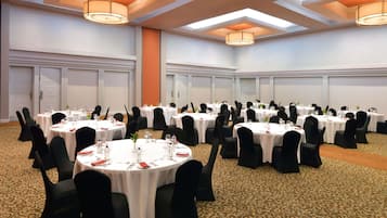 Uma sala de conferência com mesas redondas, cadeiras pretas e toalhas de mesa brancas.