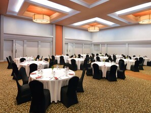 Un salón de conferencias con mesas redondas, sillas negras y manteles blancos.
