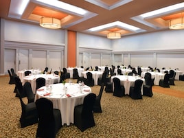 Un salón de conferencias con mesas redondas, sillas negras y manteles blancos.