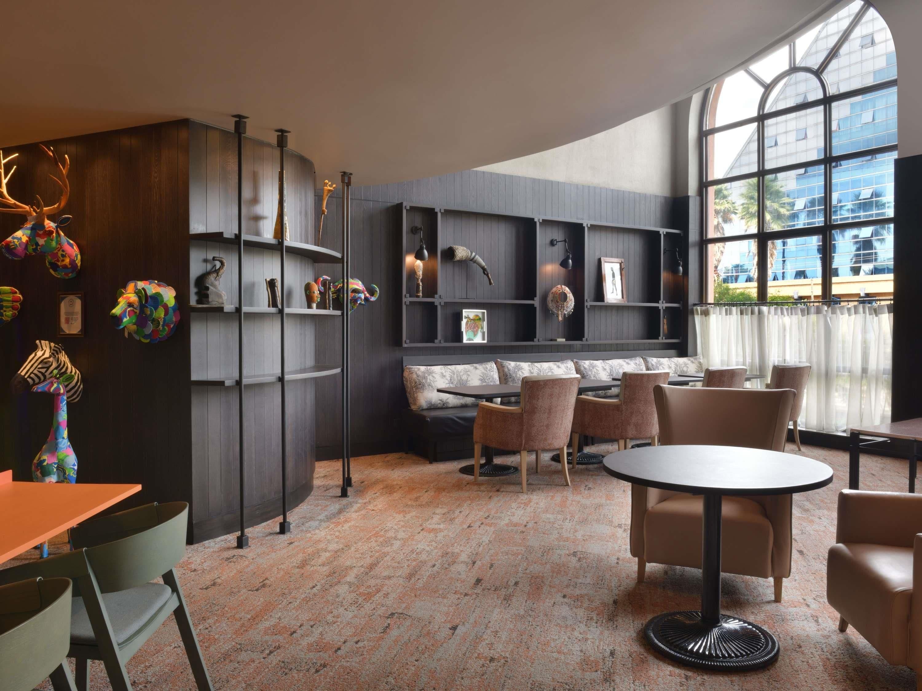 Un interior moderno con una zona de estar, una mesa redonda y un ventanal con vistas a edificios.