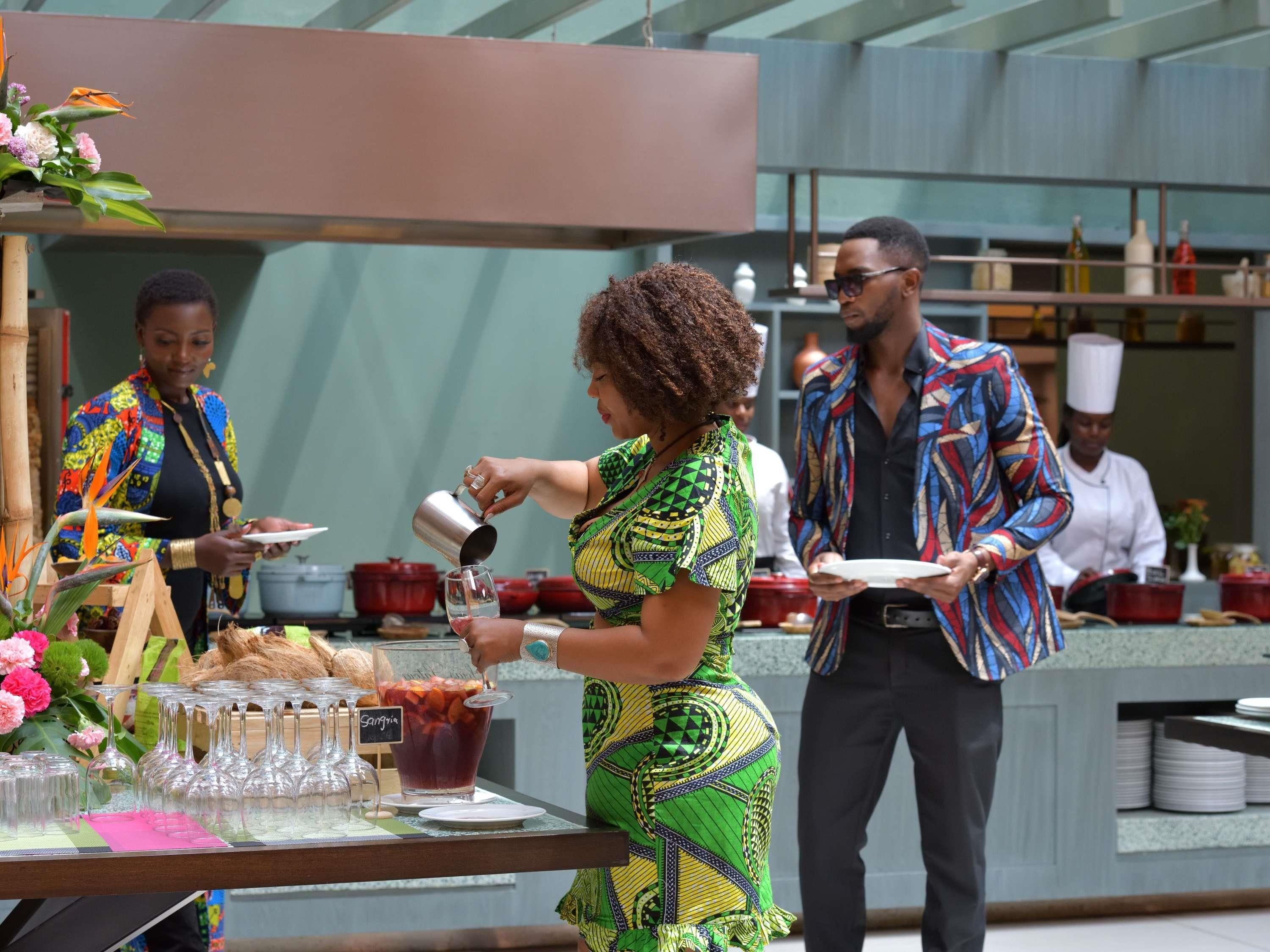 A person pouring a drink into a glass at a bar area with a counter and various kitchen items in the background.