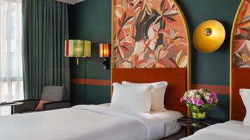 A hotel room with a bed, a chair, a lamp, a wall art piece, and a vase with flowers.