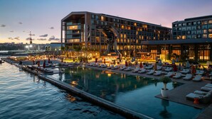 Un hôtel moderne doté d’une piscine sur le toit, d’espaces de détente et offrant une vue sur les toits de la ville au crépuscule.