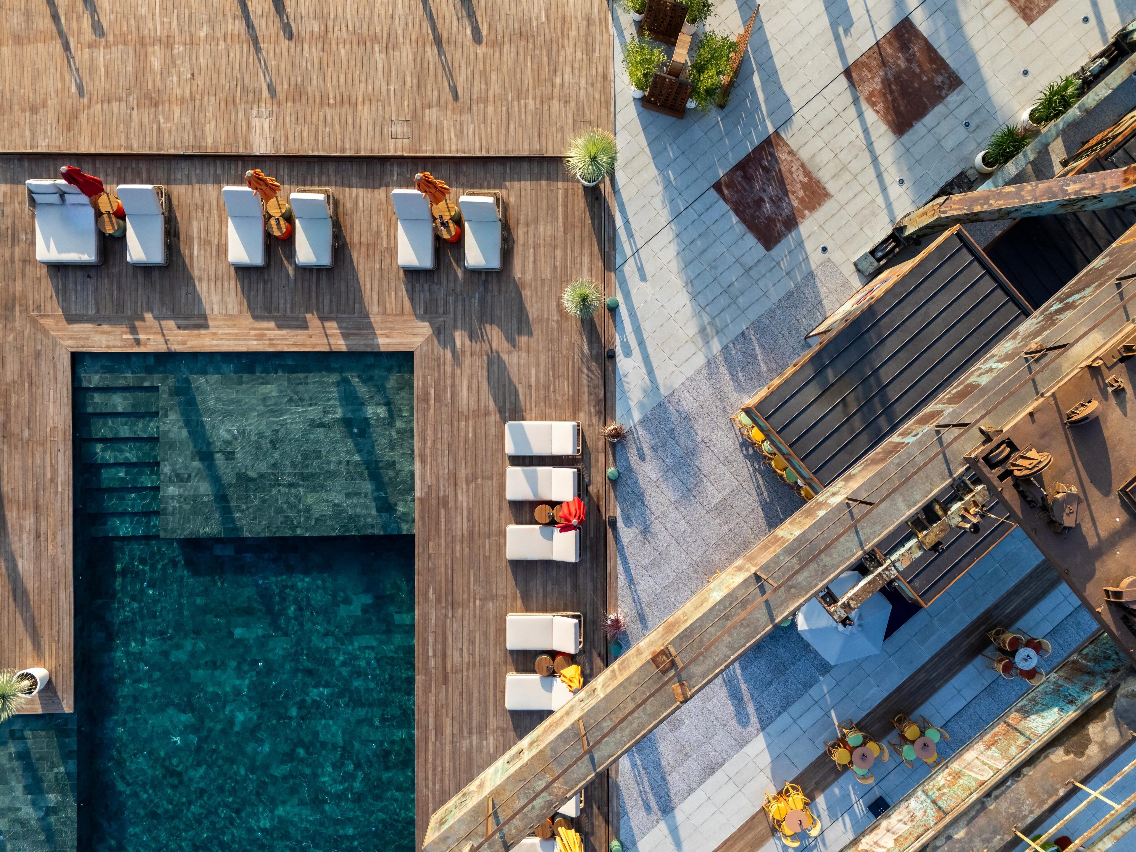 An aerial view of a rooftop pool area with multiple lounge chairs and a wooden deck.