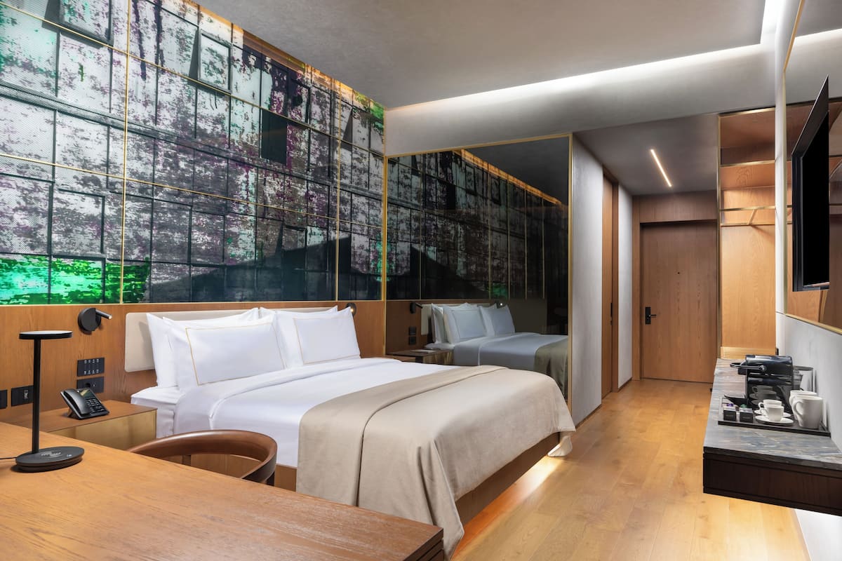 Una habitación de hotel moderna con una cama grande, un escritorio con cafetera y un ventanal con vistas a árboles.