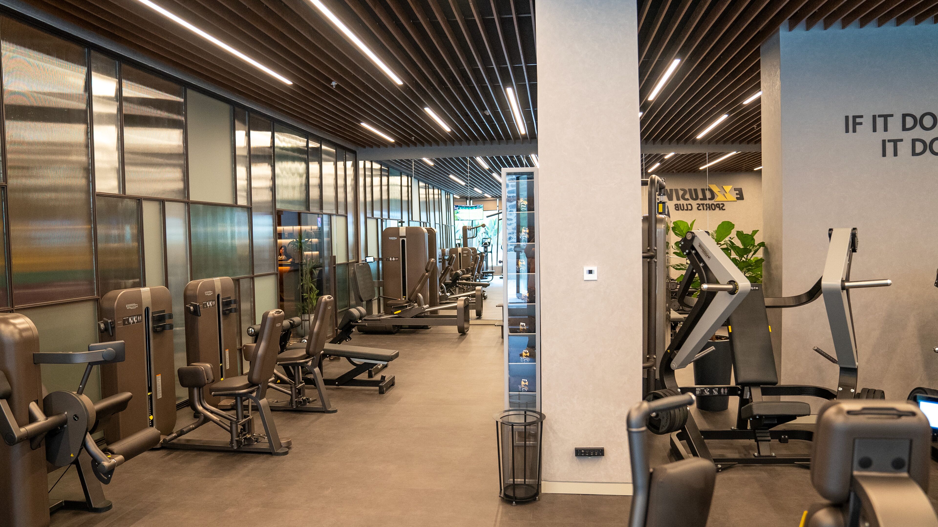 Ein Fitnessstudio mit verschiedenen Trainingsgeräten, einer Wand mit motivierenden Texten und einem großen Fenster für natürliches Licht.