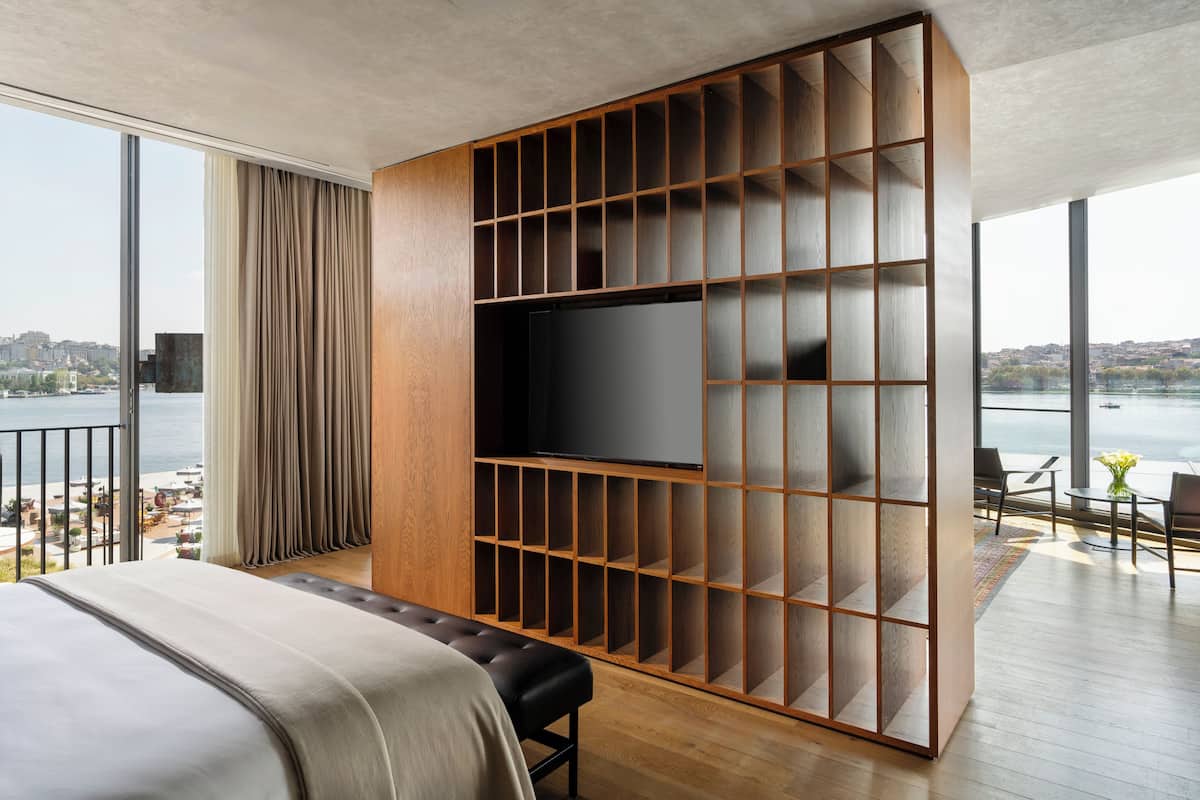Una habitación de hotel moderna con una cama grande, un televisor montado en una pared de madera y un balcón con vistas a la ciudad y al agua.