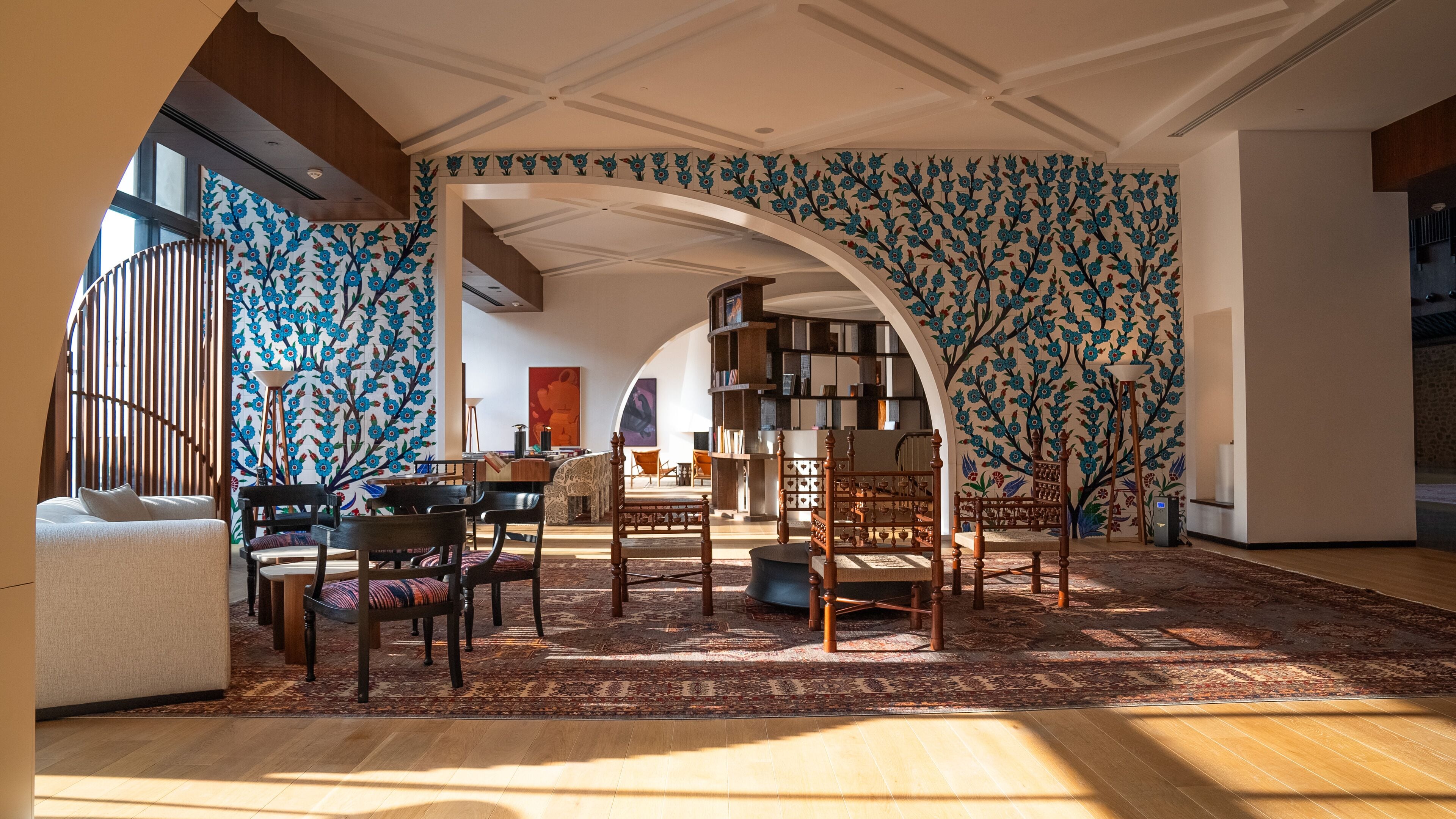 A spacious living room with a high ceiling, a large wooden bookshelf, and a patterned wall.