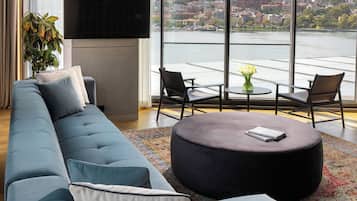 A modern living room with a large sectional sofa, a round ottoman, and a view of a cityscape through large windows.