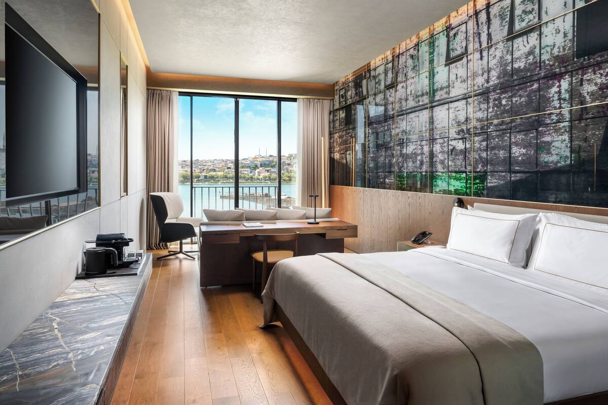 Una habitación de hotel moderna con una cama grande, un escritorio con una silla, un televisor y vistas a la ciudad.