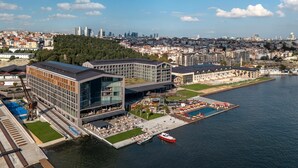 A waterfront hotel with modern architecture, a pool area, and a view of the city skyline.