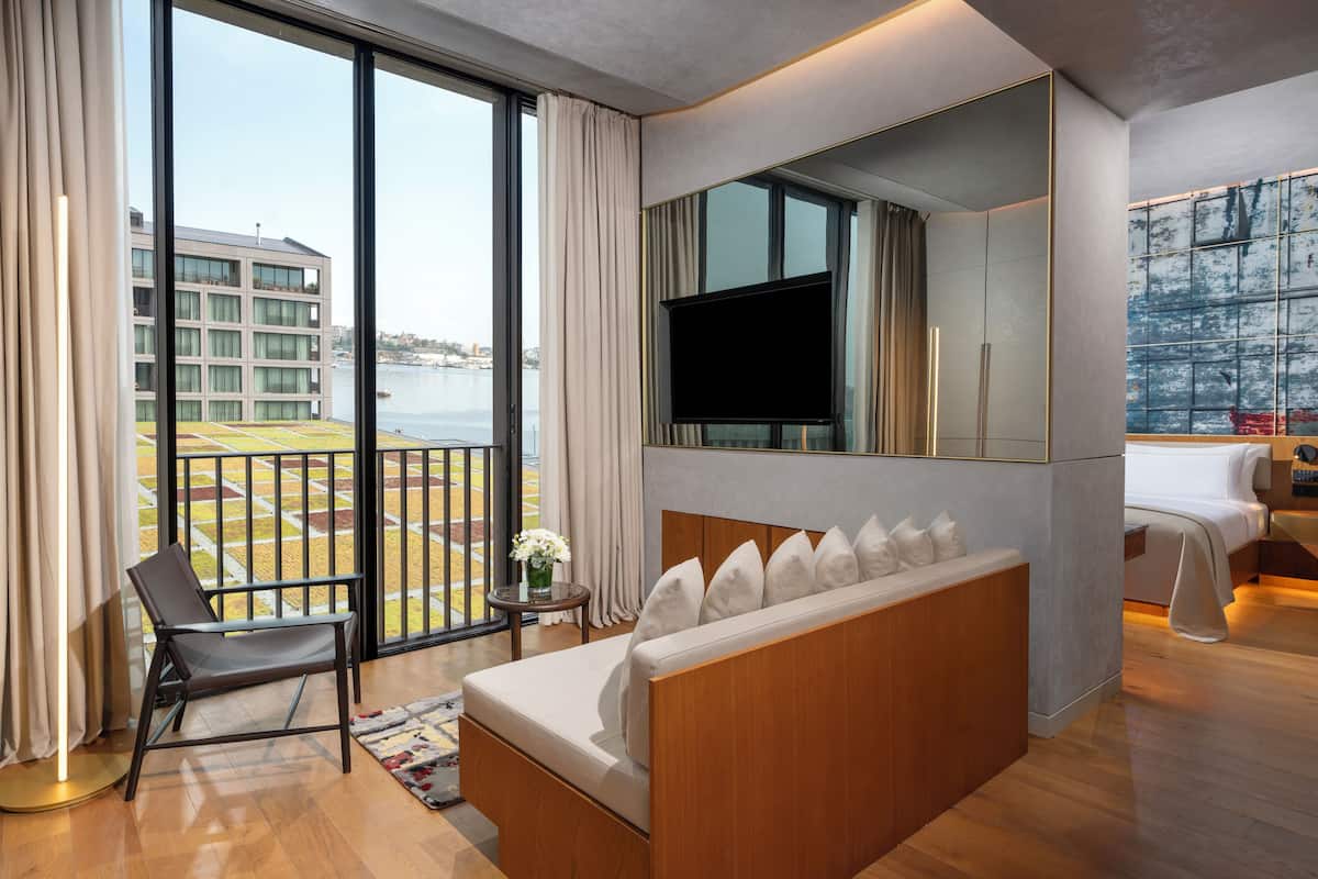Una habitación de hotel moderna con un ventanal grande, un sofá, un televisor y una cama.