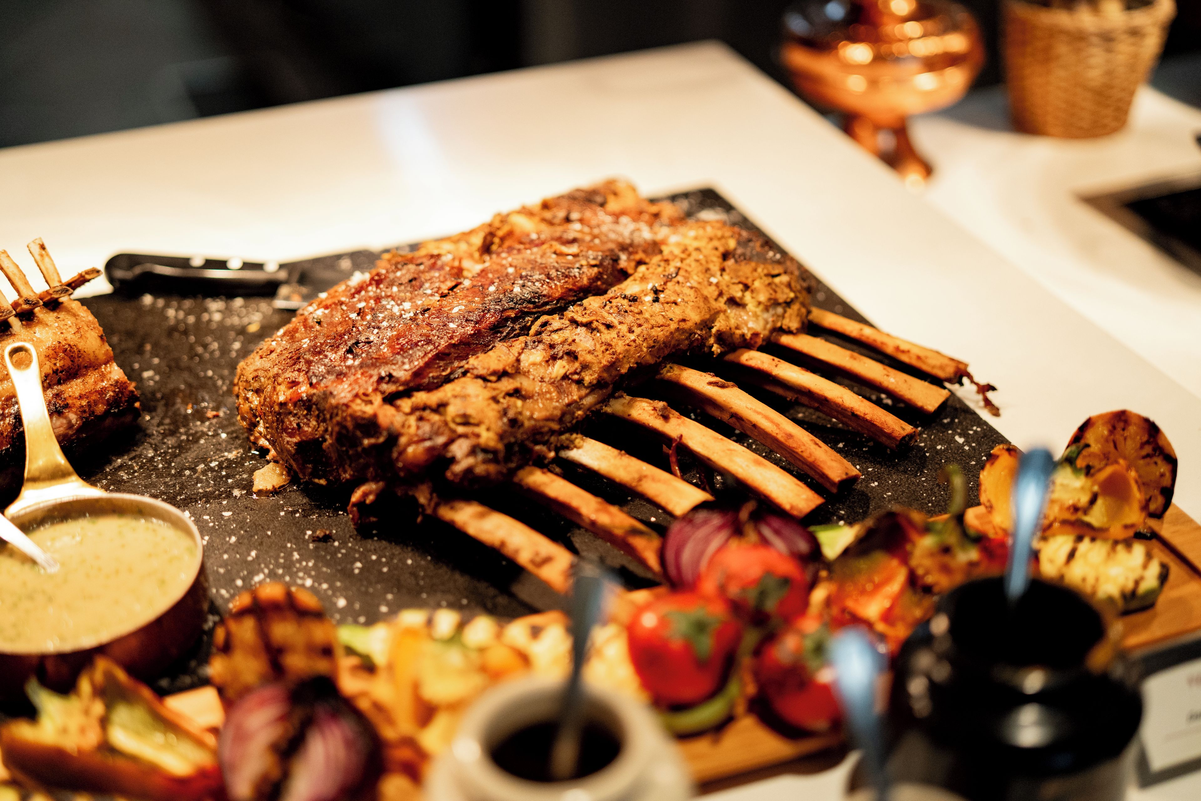 A rack of meat with vegetables and sauce on a table.