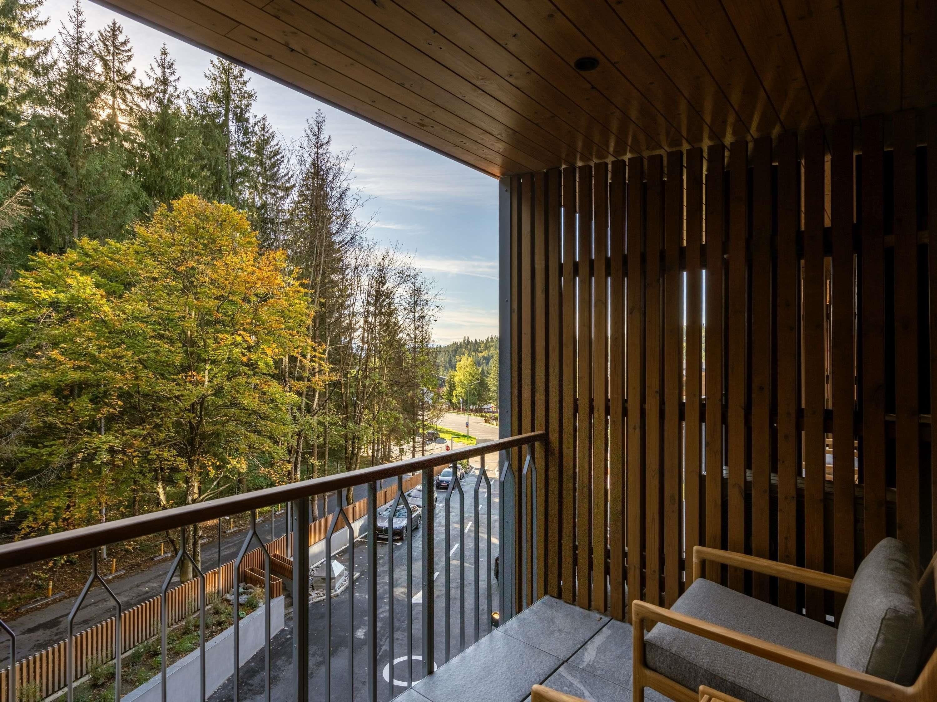 A balcony with a view of a road and trees, a chair, and a wooden slatted wall.