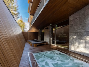 Zona de spa con terraza de madera, paredes de piedra y bañera de hidromasaje.