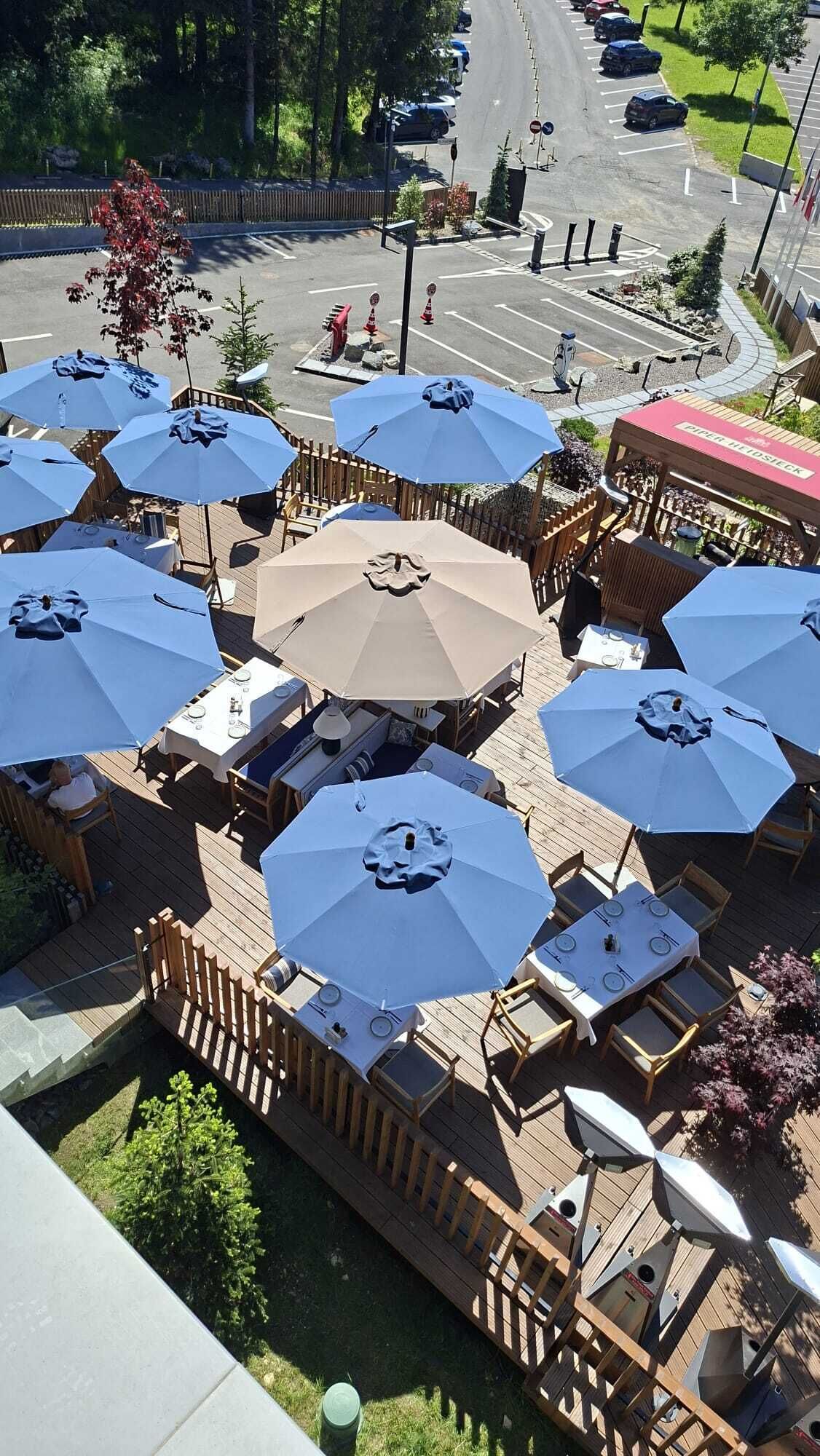Un restaurante al aire libre con varias mesas y sombrillas, rodeado por una terraza de madera y vistas a una carretera.