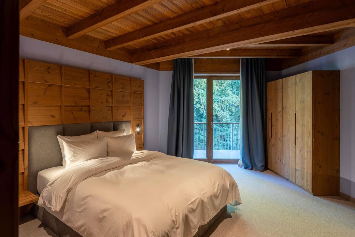 Ein Schlafzimmer mit Holzboden, einem großen Bett, einem Kleiderschrank und einem Fenster mit Vorhängen.