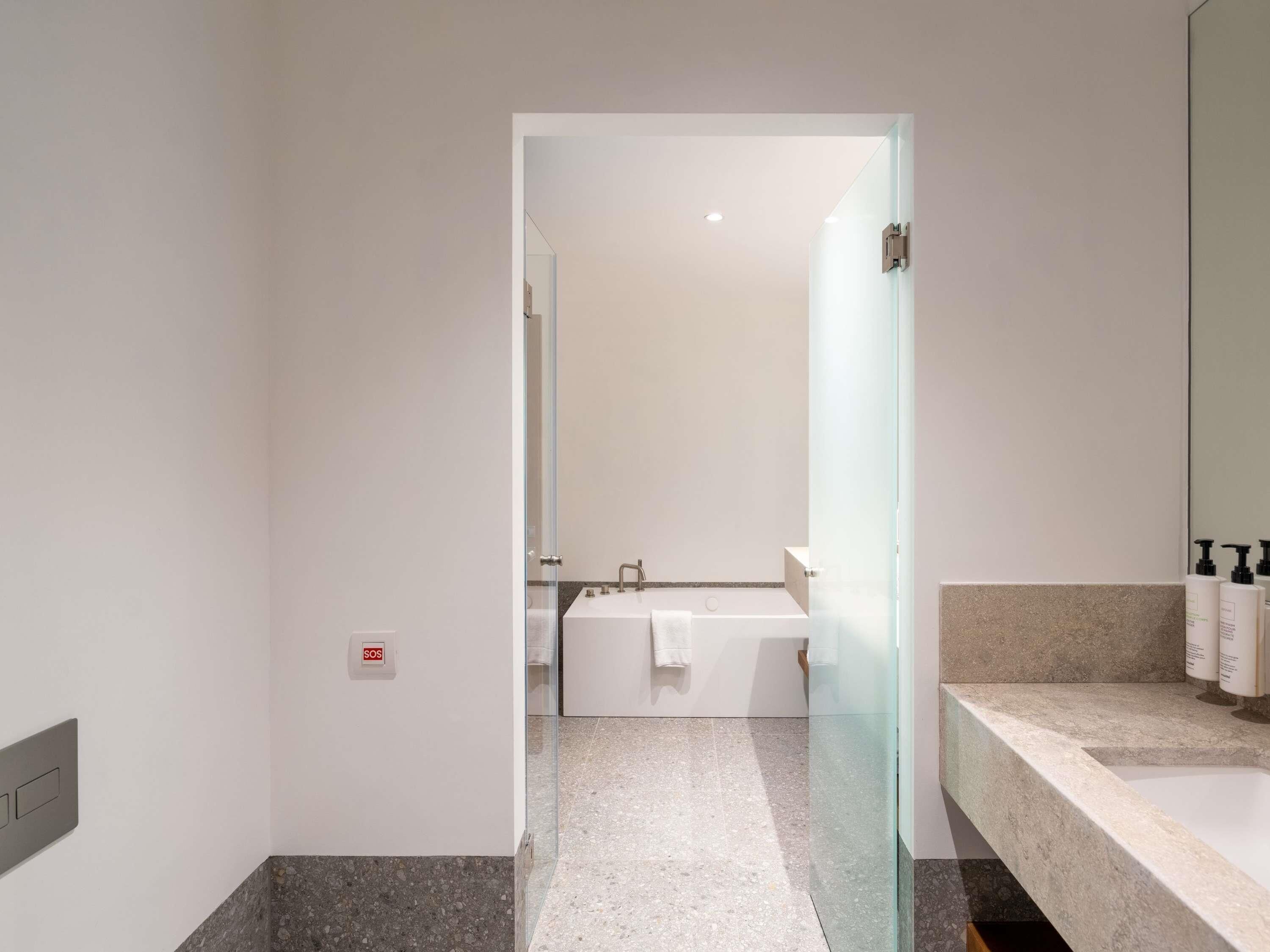 Een moderne badkamer met een glazen deur naar een douchegedeelte, een grote spiegel en een aanrecht met toiletartikelen.