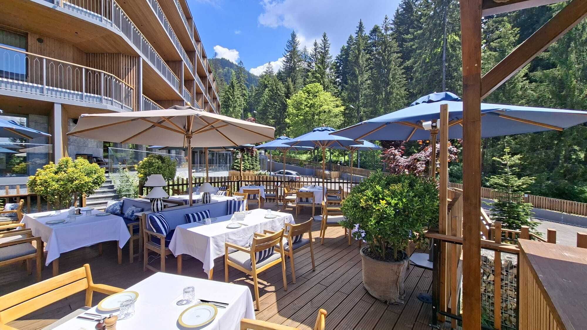 Un espace de restauration en plein air, avec des tables et des chaises, des parasols et une vue sur une chaîne de montagnes boisée.