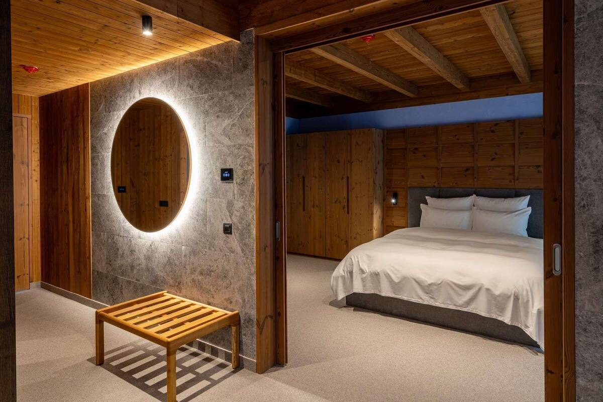 Une chambre avec un lit, un banc en bois, un luminaire rond et un mur en pierre.