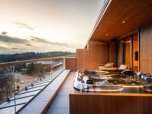 Ein Balkon mit Whirlpool, Holzverkleidung und Blick auf ein bewaldetes Gebiet.