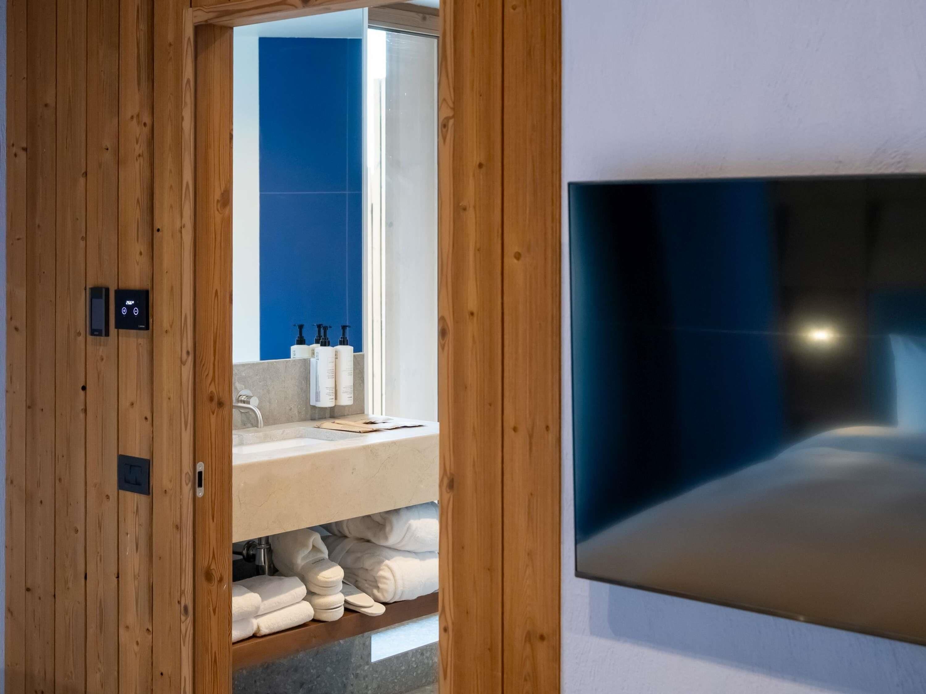 Une salle de bain moderne avec un décor de panneaux en bois, un mur recouvert de carreaux bleus, un lavabo avec des articles de toilette et un grand miroir.