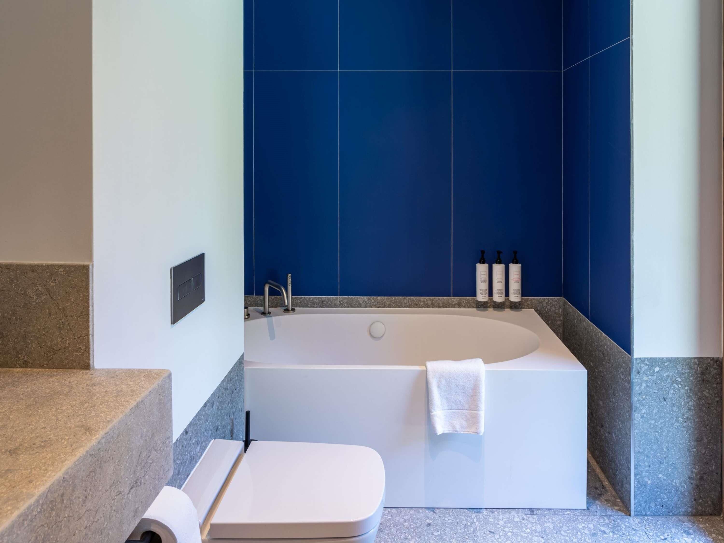 A modern bathroom with a freestanding bathtub, a towel rack, and toiletries on the wall.