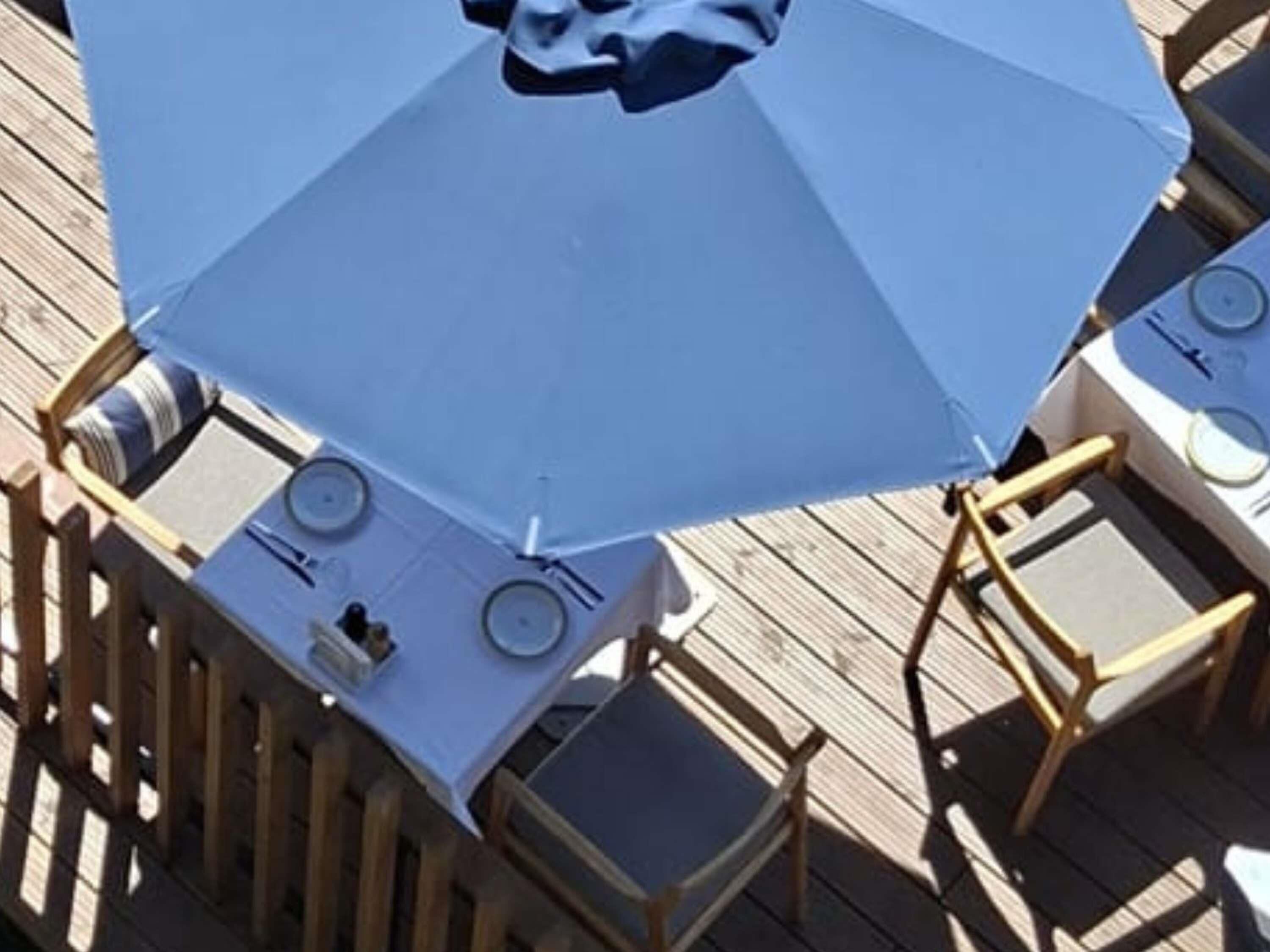 A deck with outdoor seating, including tables and chairs, and a large umbrella providing shade.