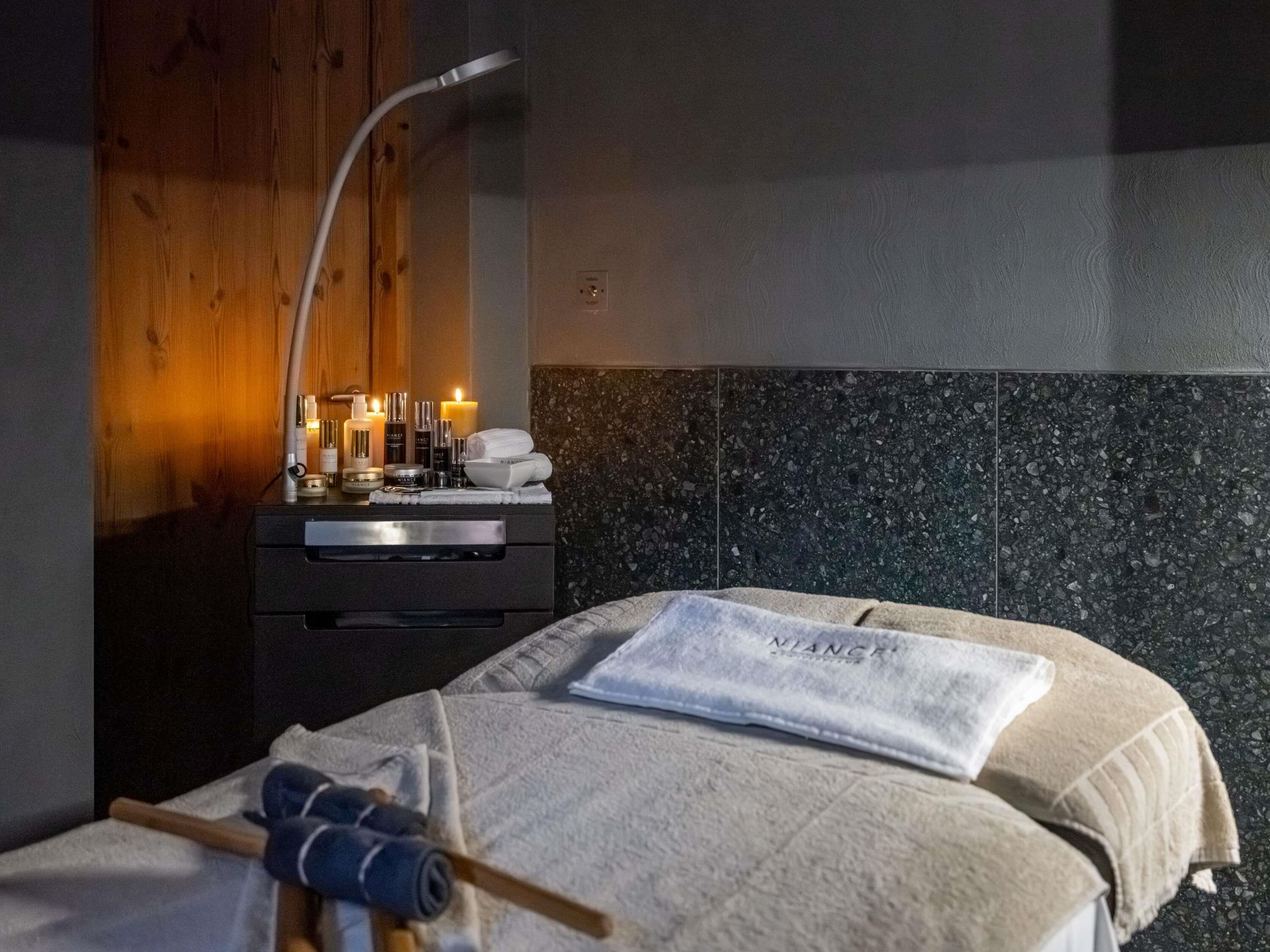 A hotel room with a bed, a nightstand with toiletries, a wooden wall, and a tiled headboard.