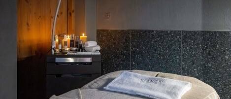 A hotel room with a bed, a nightstand with toiletries, a wooden wall, and a tiled headboard.