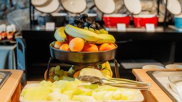 A buffet with various fruits and vegetables, a stone wall background, and a metal rack with plates.
