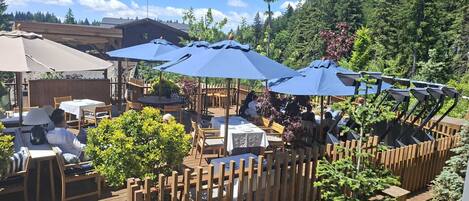 Un espace extérieur aménagé en terrasse, avec des tables et des chaises en bois, des parasols et une clôture en bois.