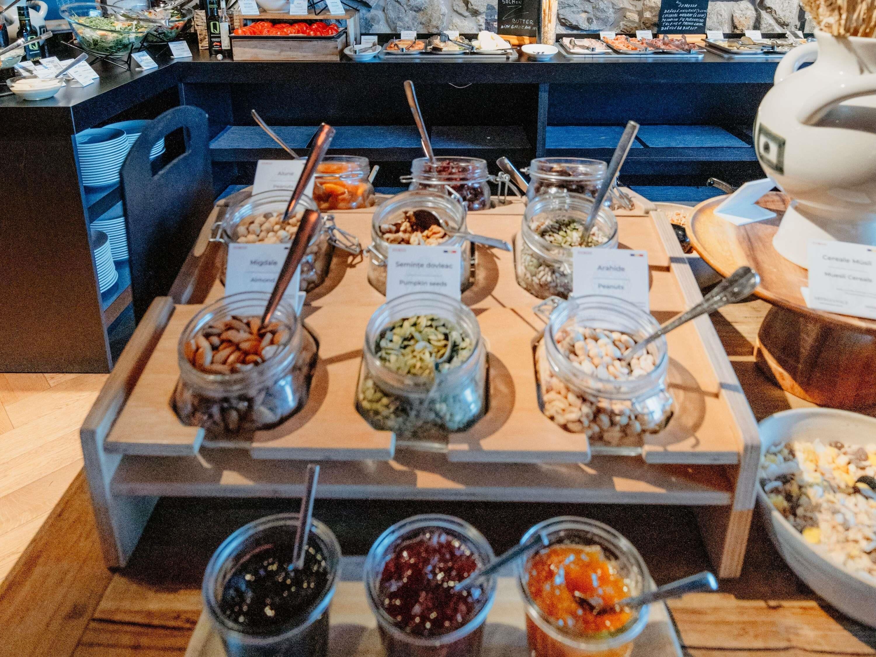A buffet with various food items in jars and bowls, including nuts, fruits, and salads.