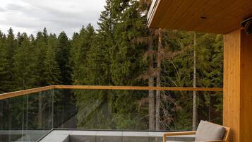 A balcony with a glass railing, a wooden chair, and a view of a forest.
